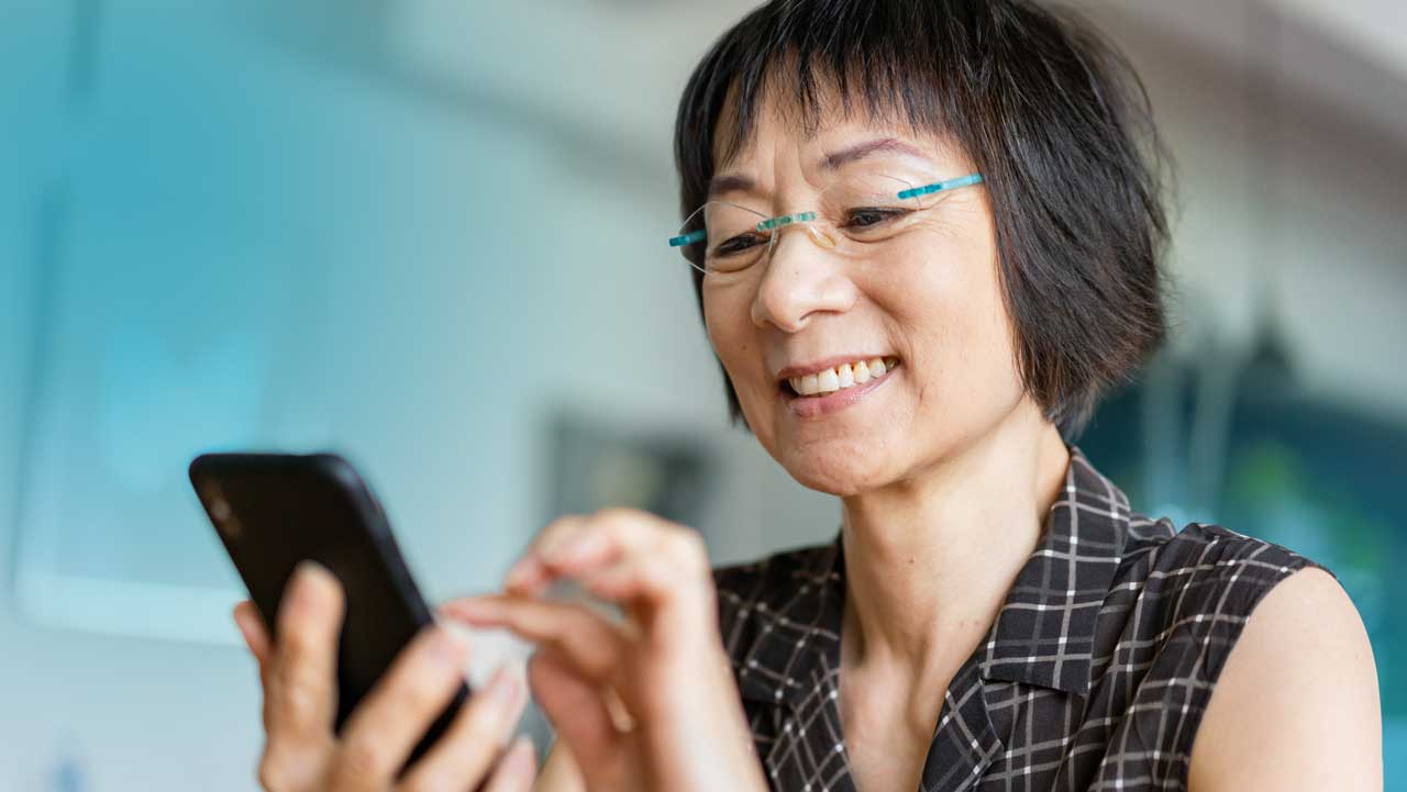 Smiling woman with short black hair and glasses using a smartphone indoors.